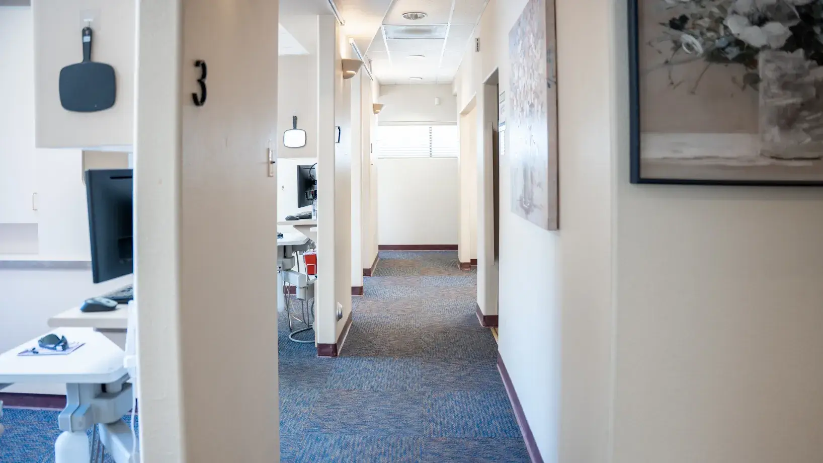 A hallway in a medical or dental office with rooms on both sides and equipment visible.