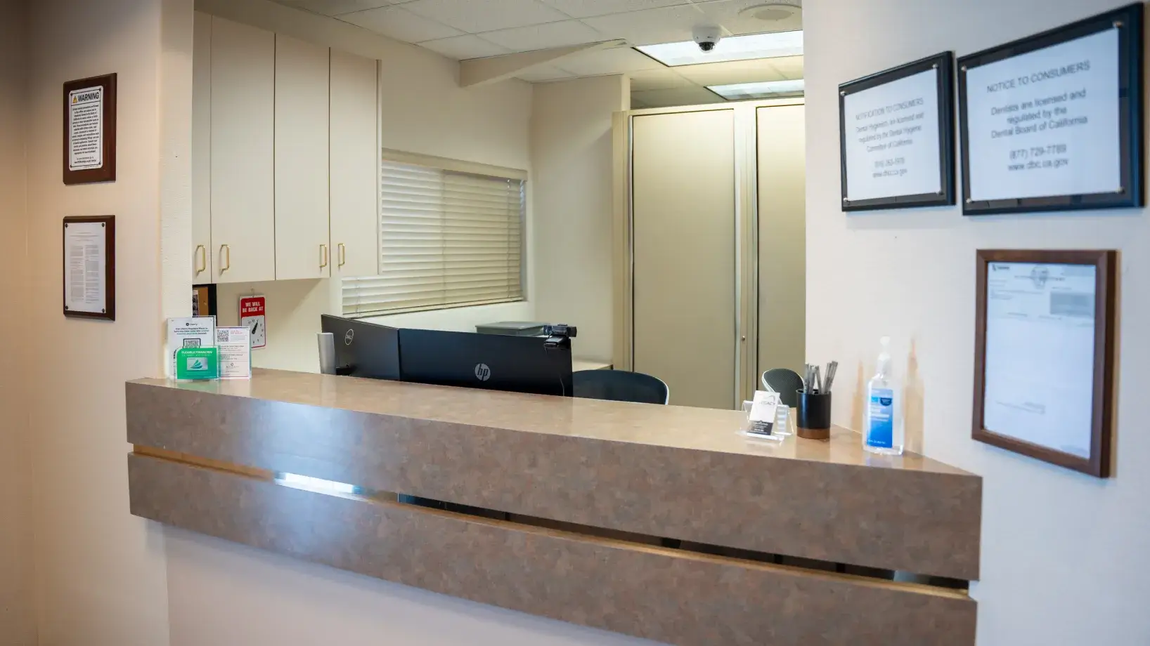 A small, empty reception desk with office supplies and a hand sanitizer bottle on the counter.
