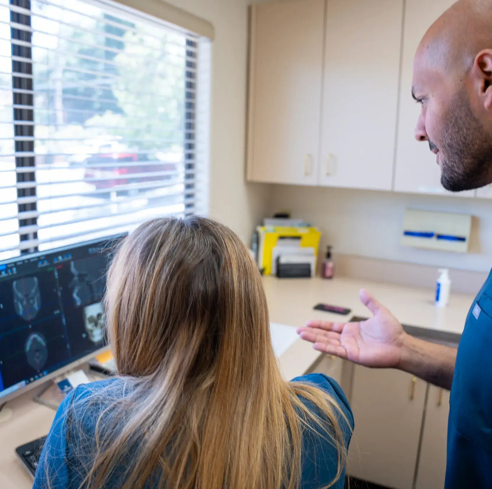 A person shows another person brain scans on a computer screen in an office.