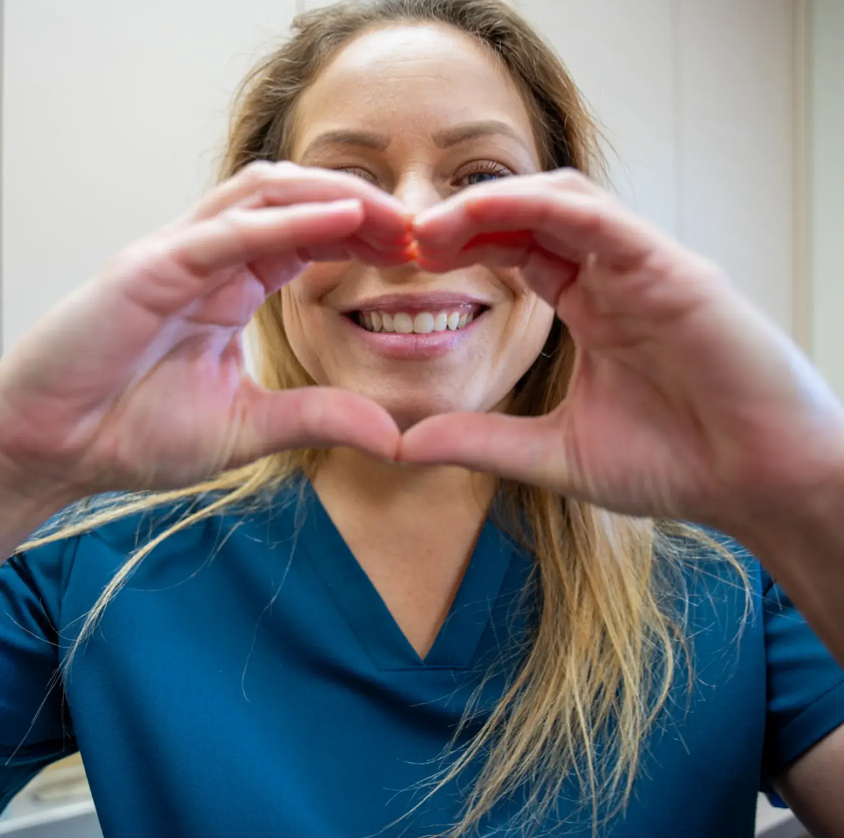 A person in a blue shirt makes a heart shape with their hands, smiling.