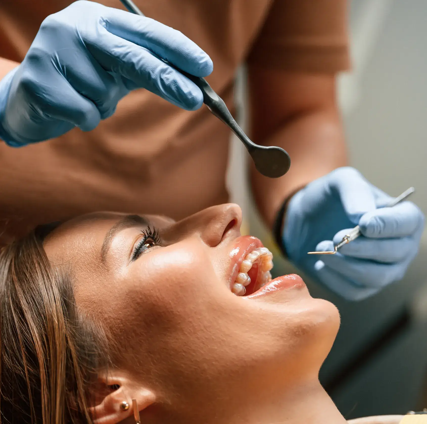 A dentist wearing gloves examines a smiling patient's teeth with dental tools.