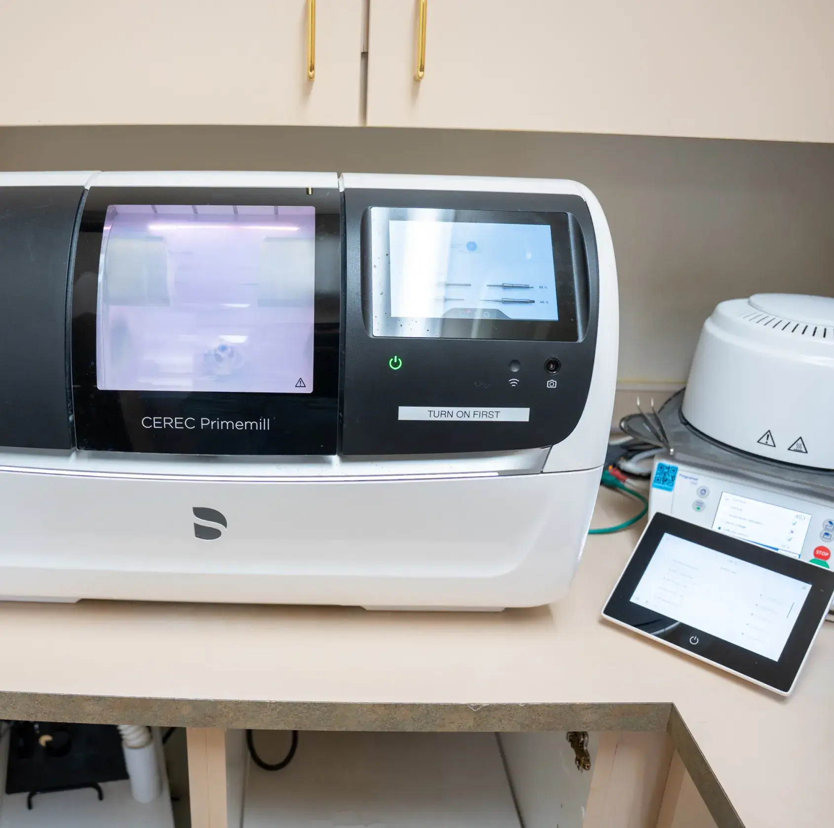 A dental milling machine with screens and controls sits on a countertop in a clinic.