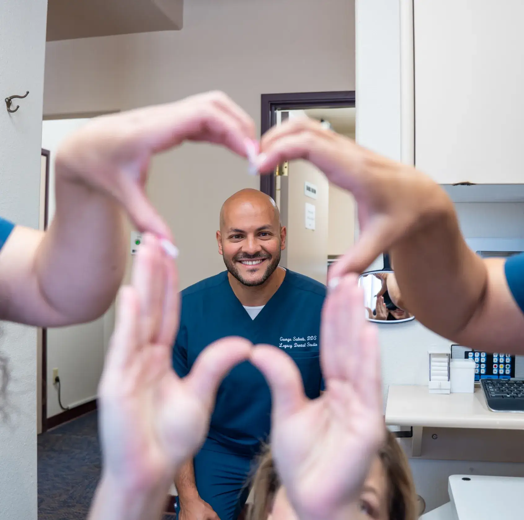 Two people form a heart shape with their hands; a person in scrubs smiles in the center.