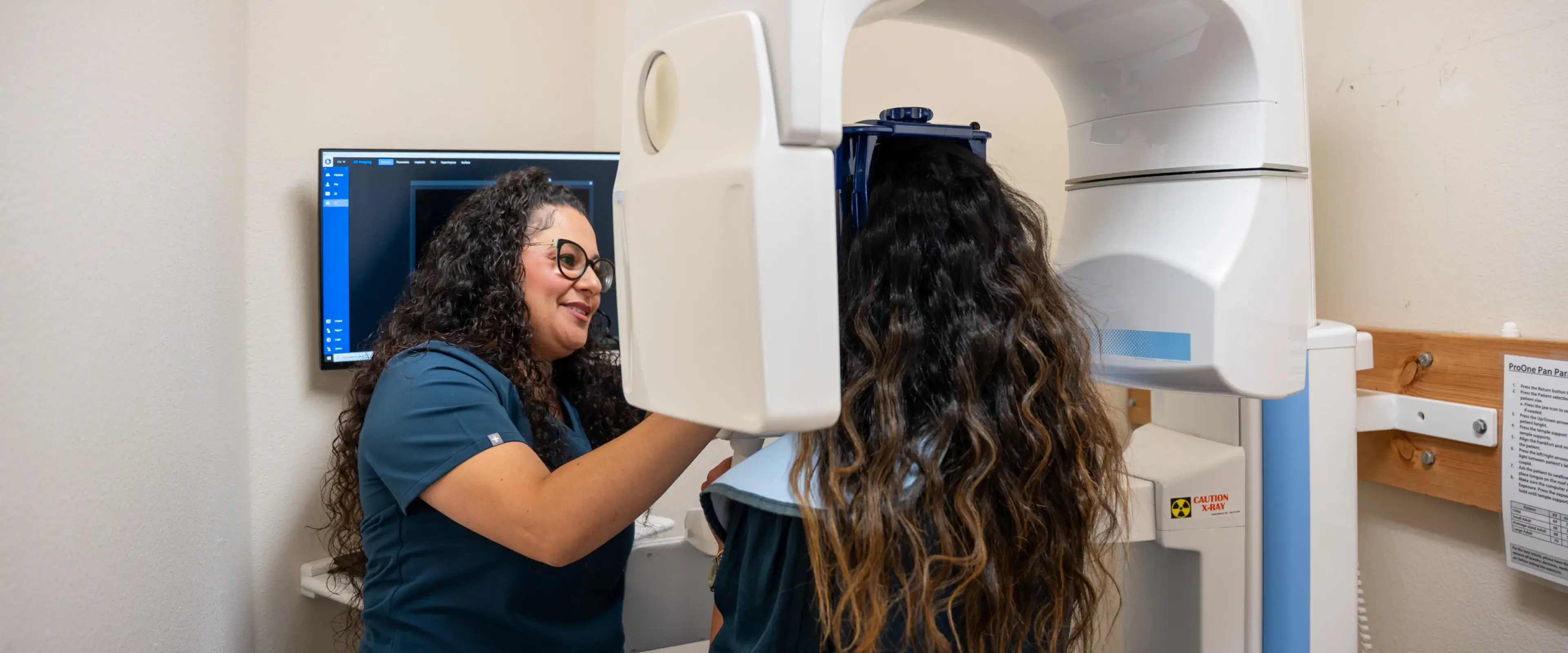 A dental technician assists a patient with a panoramic dental X-ray machine.