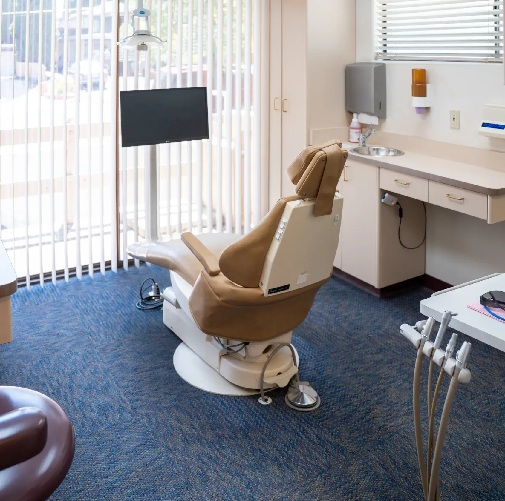 A dentist's chair in an examination room with a monitor and dental tools nearby.