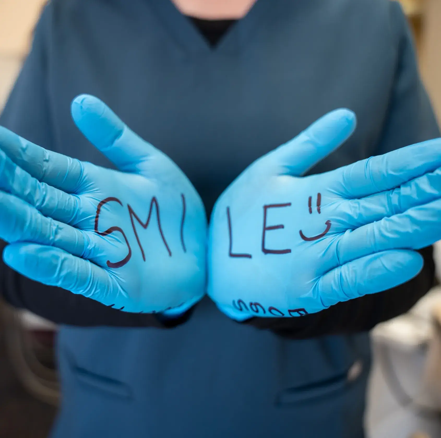 Person wearing blue gloves with the word "SMILE" written across both hands.