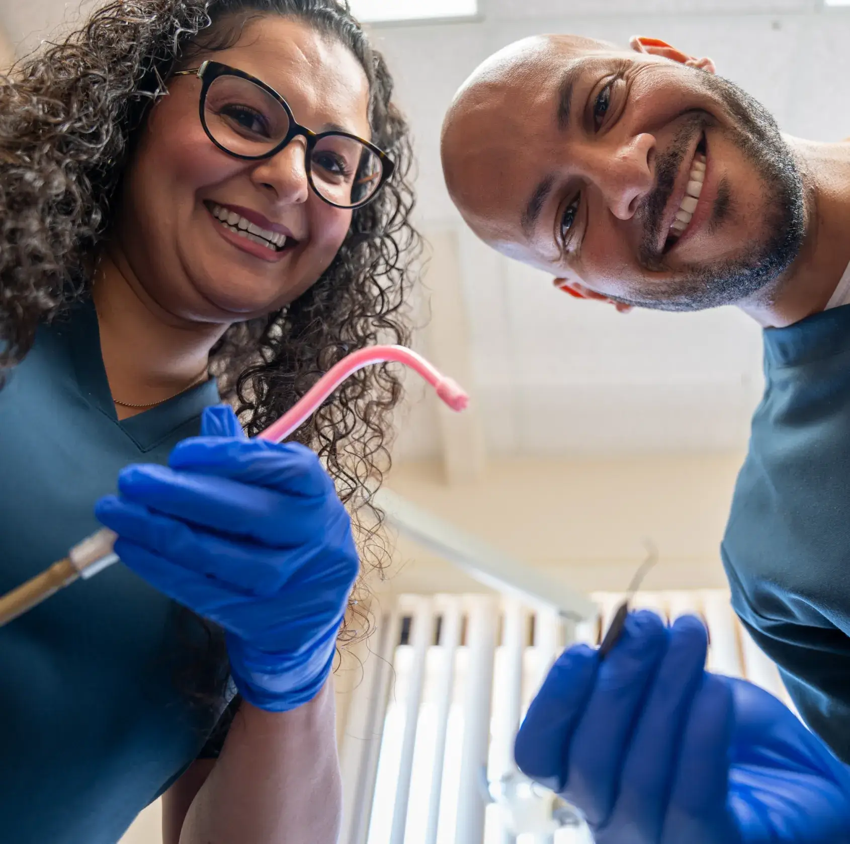 Two dental professionals wearing gloves are smiling as they prepare to treat a patient.