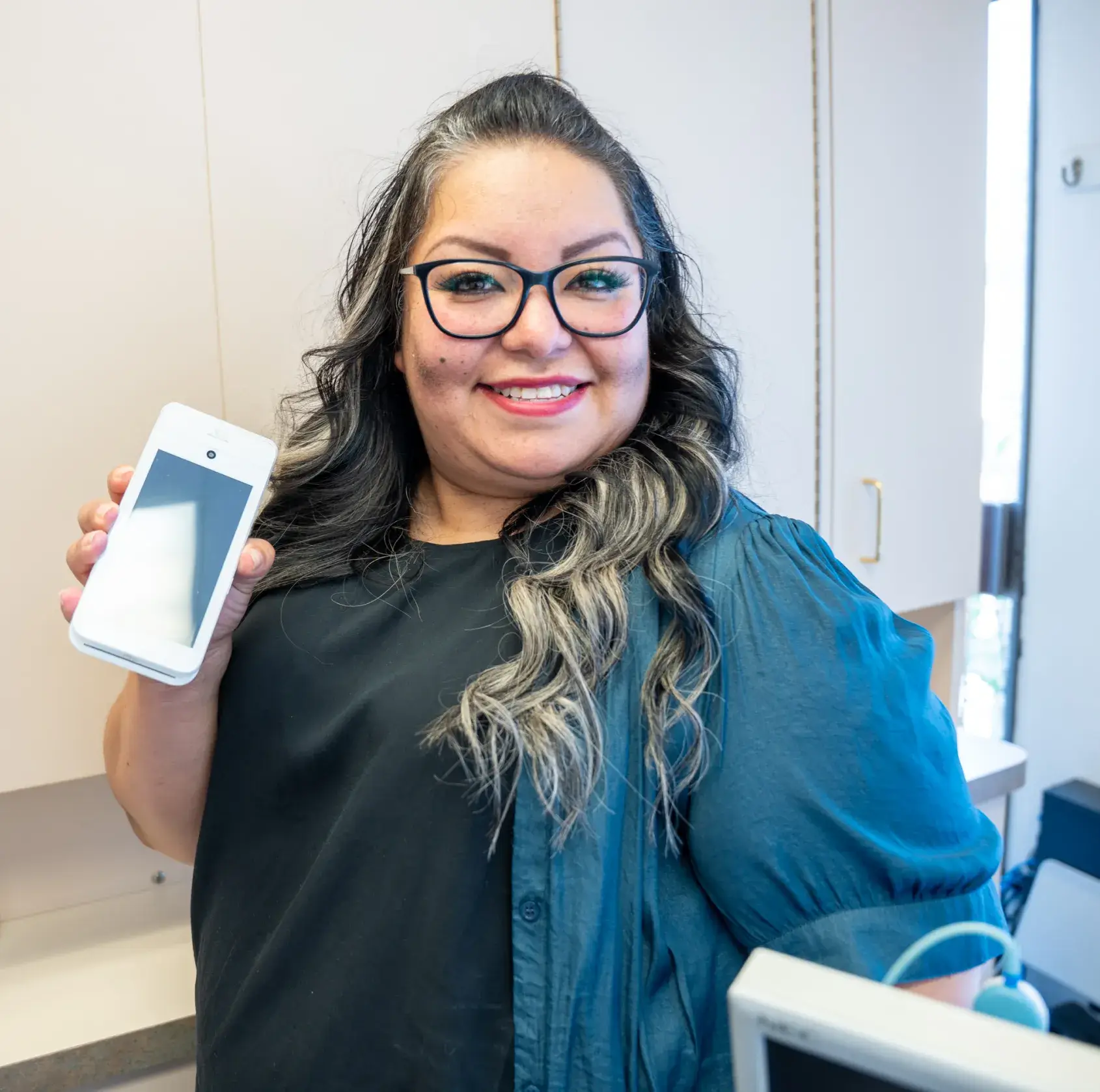 Person smiling while holding up a smartphone in an indoor setting.