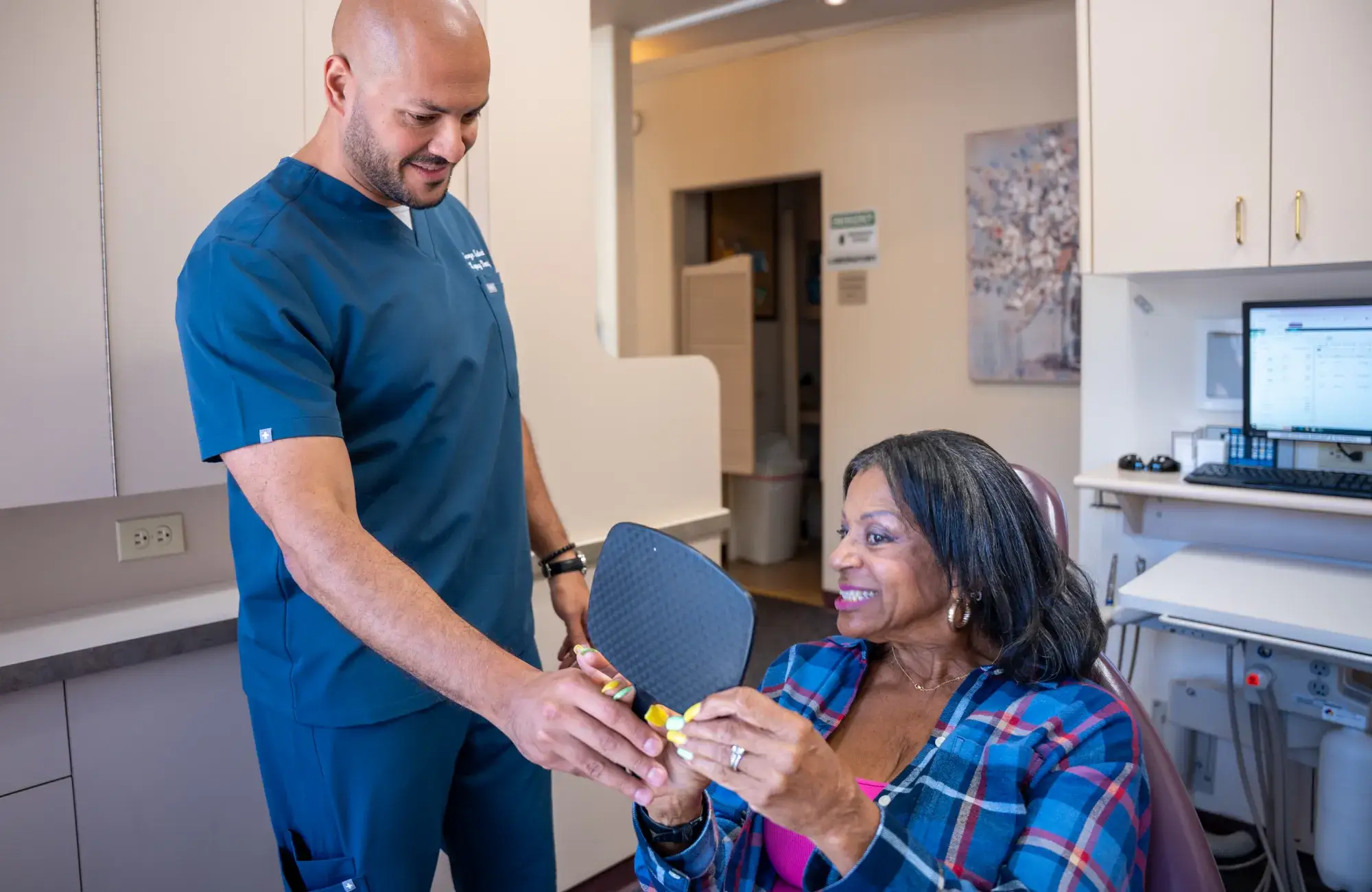 A dentist hands a mirror to a seated woman in a dental office.