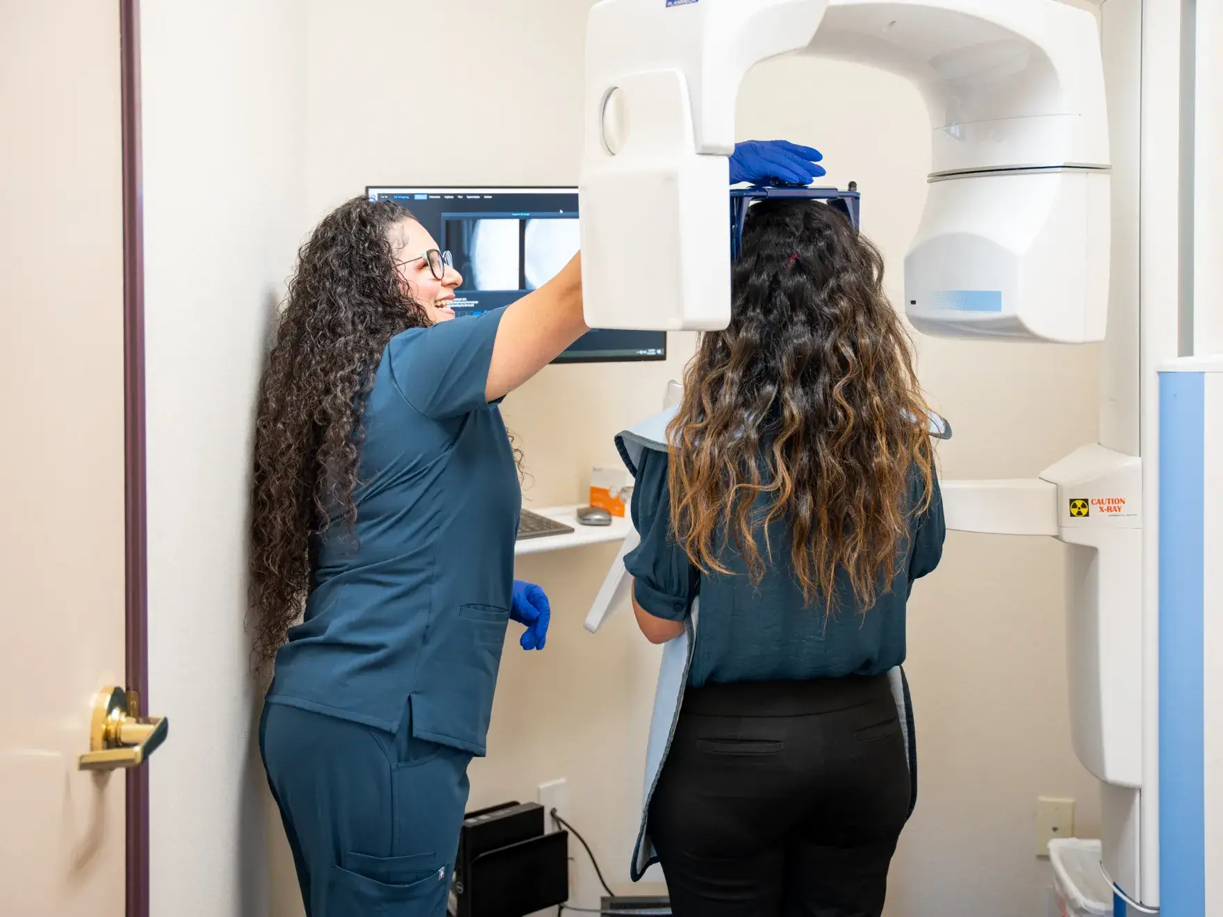 A dental assistant helps a patient positioned for an X-ray in a dental office.