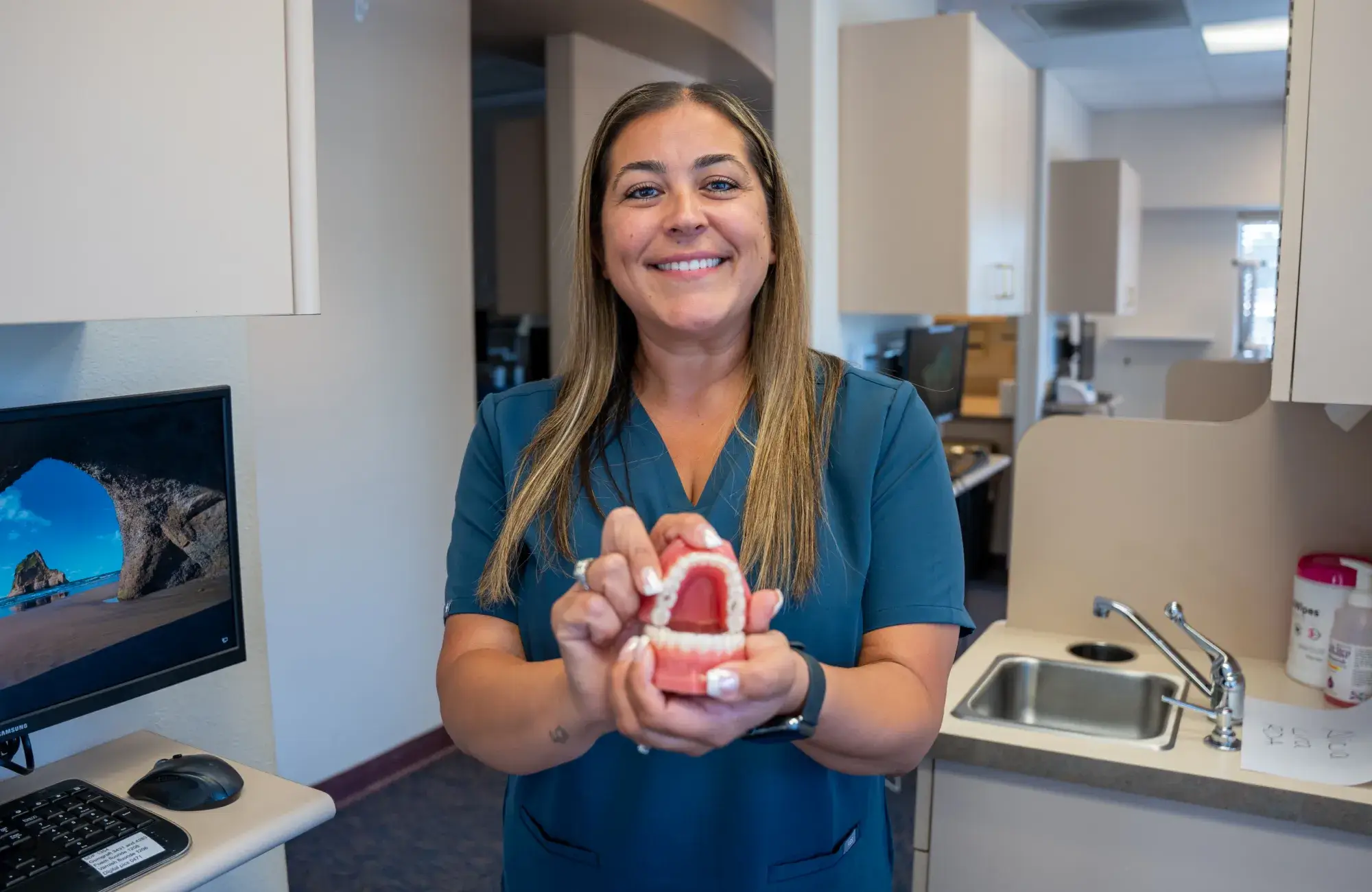 A woman smiling and holding a dental model in a dental office.