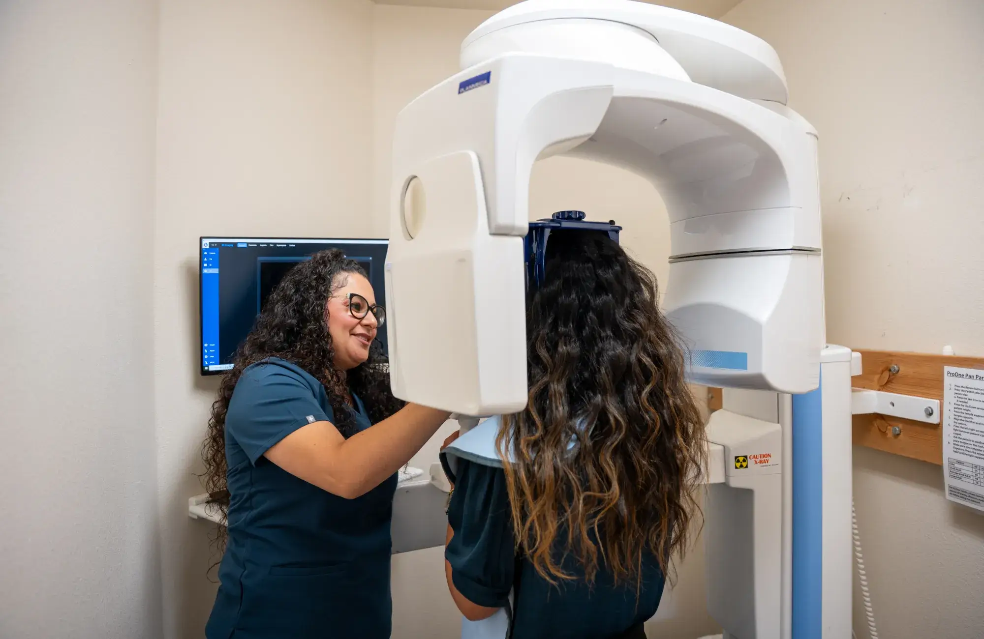 A dental technician assists a patient using a panoramic X-ray machine in a dental office.