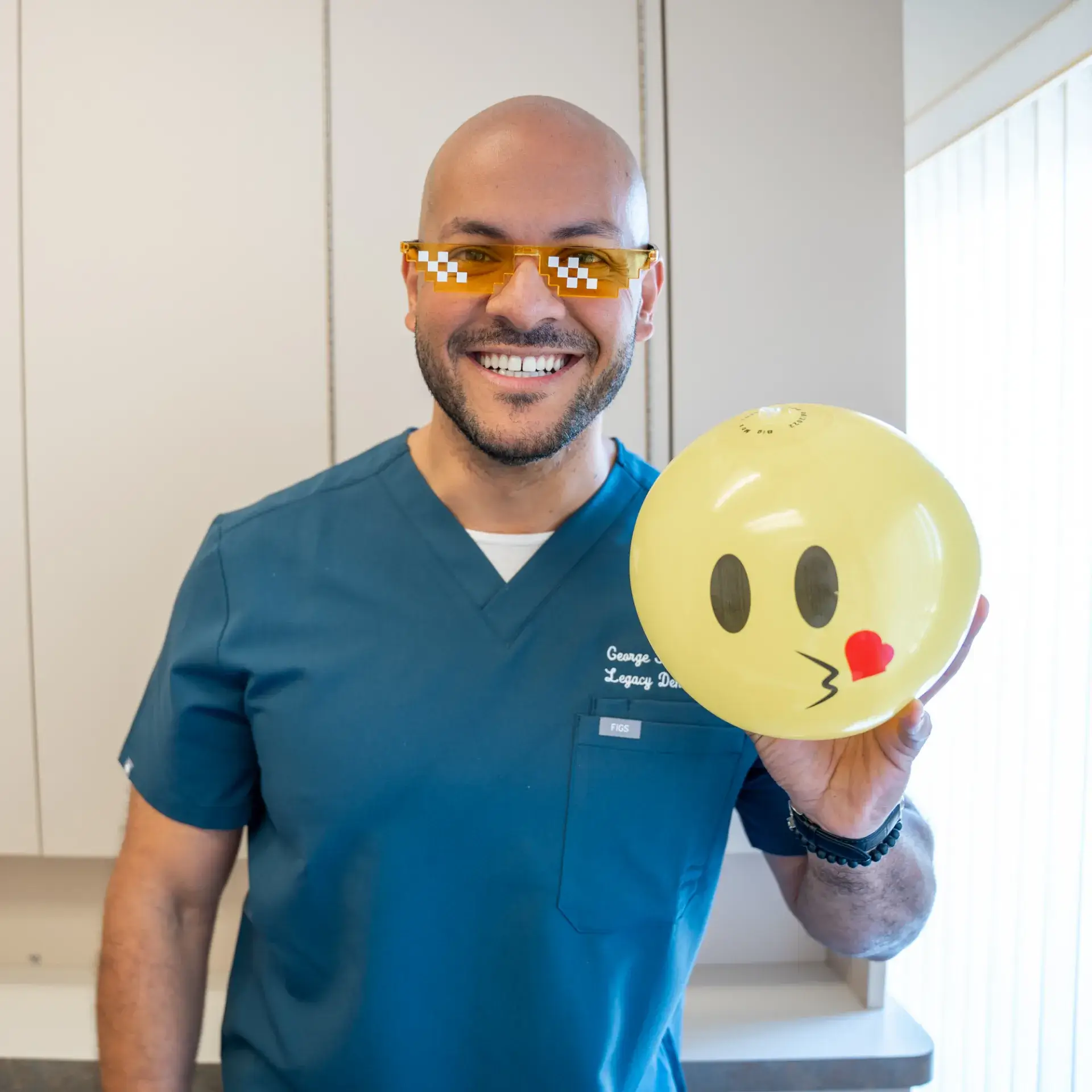 Man wearing orange glasses holding a yellow emoji balloon with a kissing face.