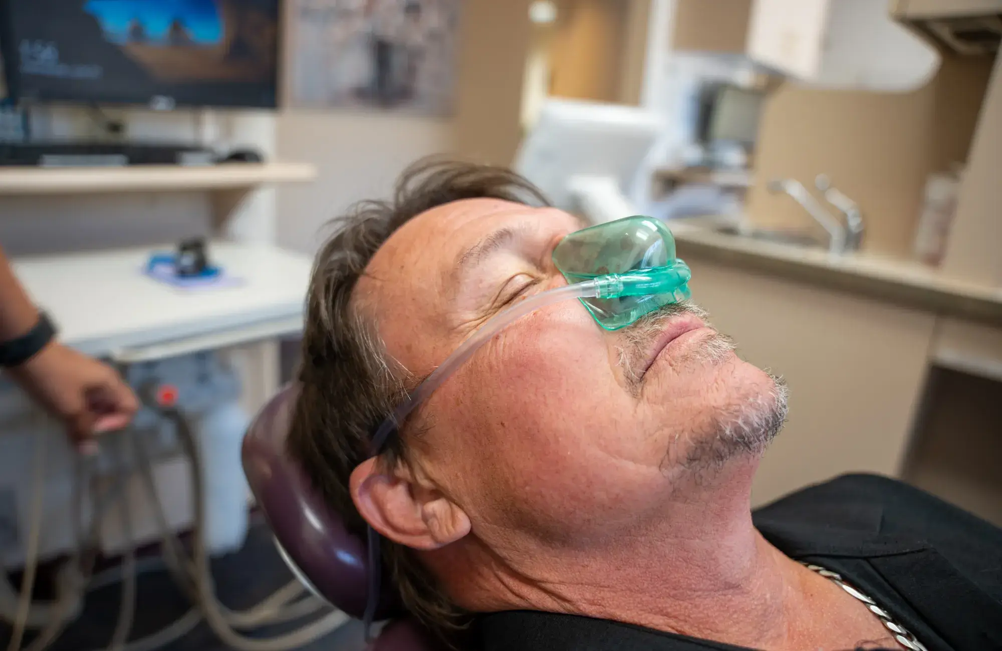 Man in dentist chair receiving nitrous oxide gas through a mask over his nose.
