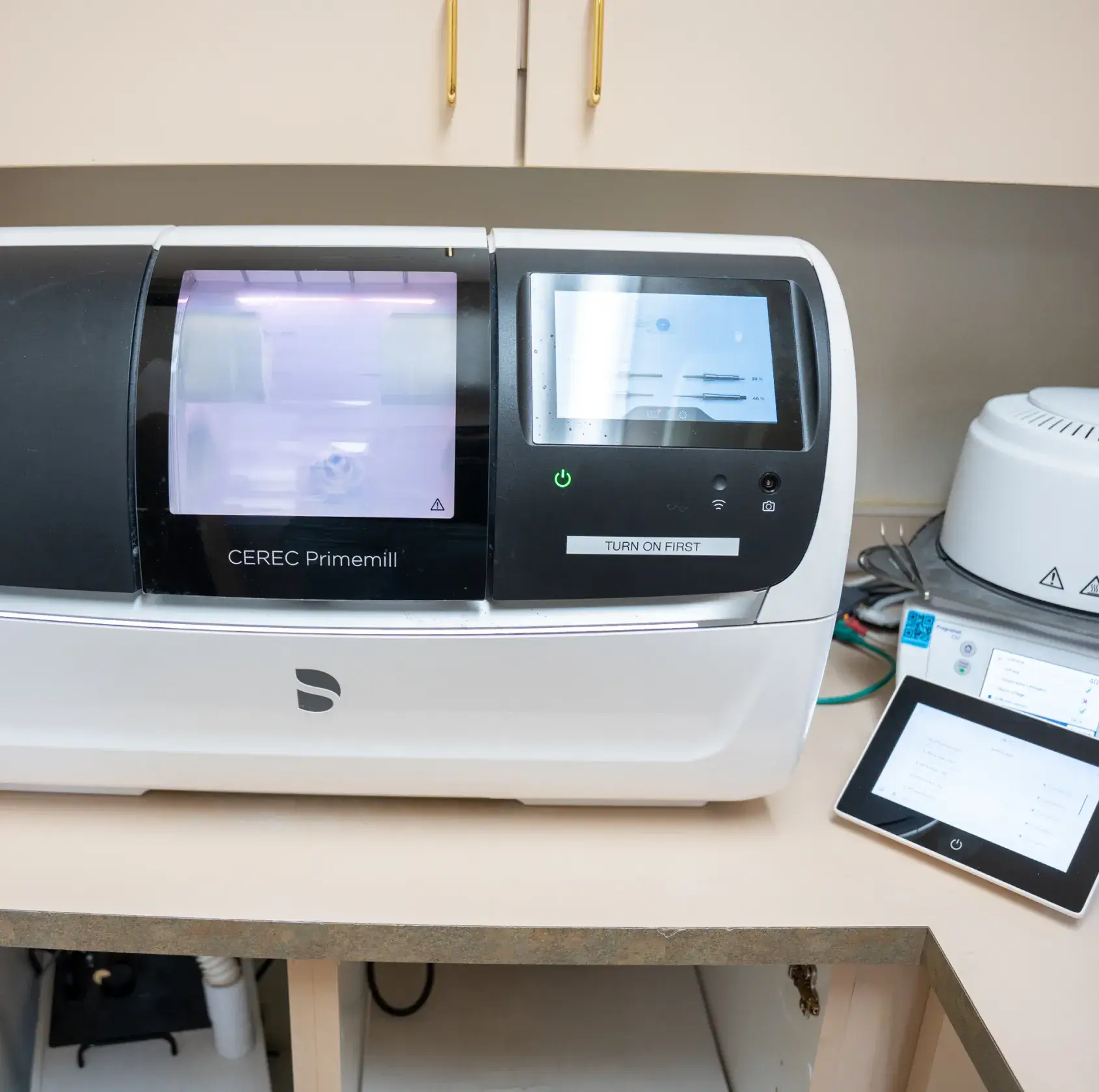 A digital dental milling machine with touchscreens displaying settings is placed on a countertop.