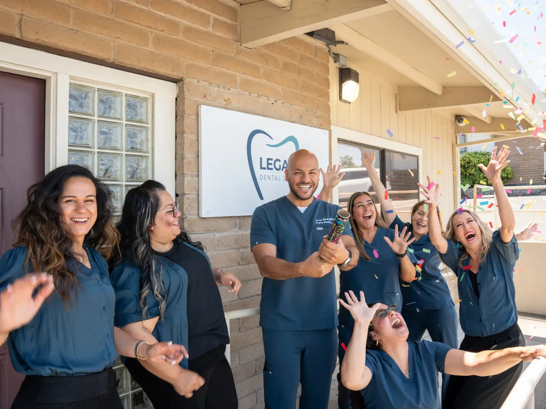 A group of dental professionals celebrates outside a clinic, with one person holding a champagne bottle.