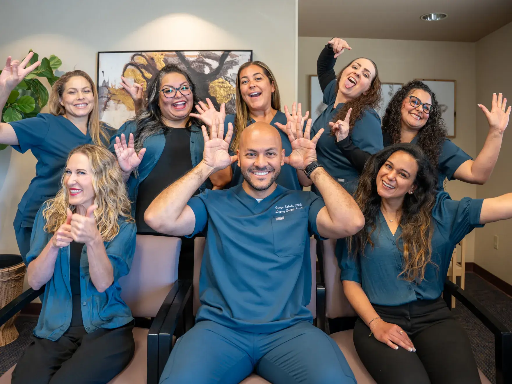 A group of eight people in matching outfits smiling and making playful hand gestures in an office setting.