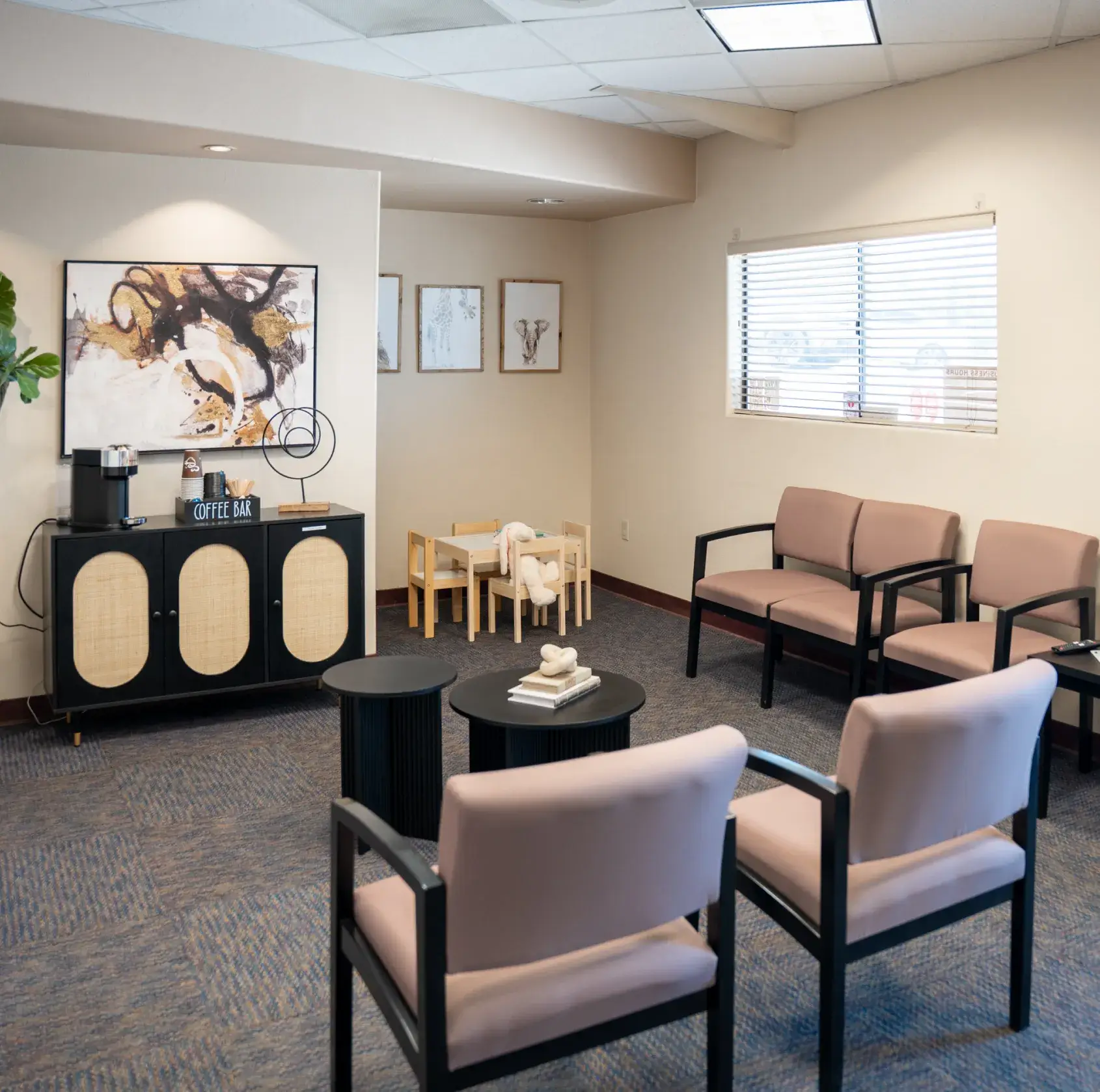 Waiting room with pink chairs, a coffee station, children's play area, and artwork on the walls.
