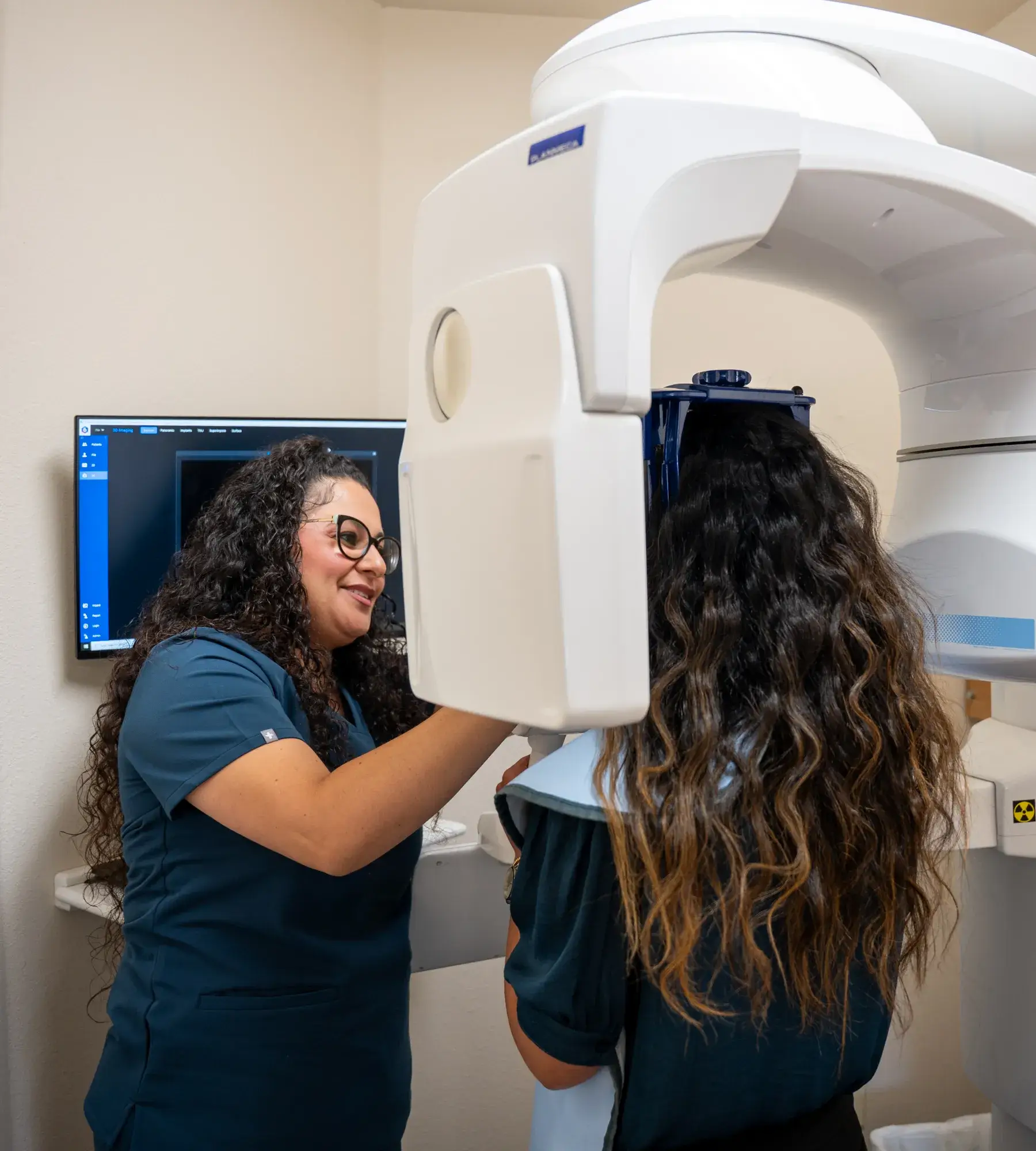 A dental technician assists a patient with a 3D dental imaging machine in a clinic.