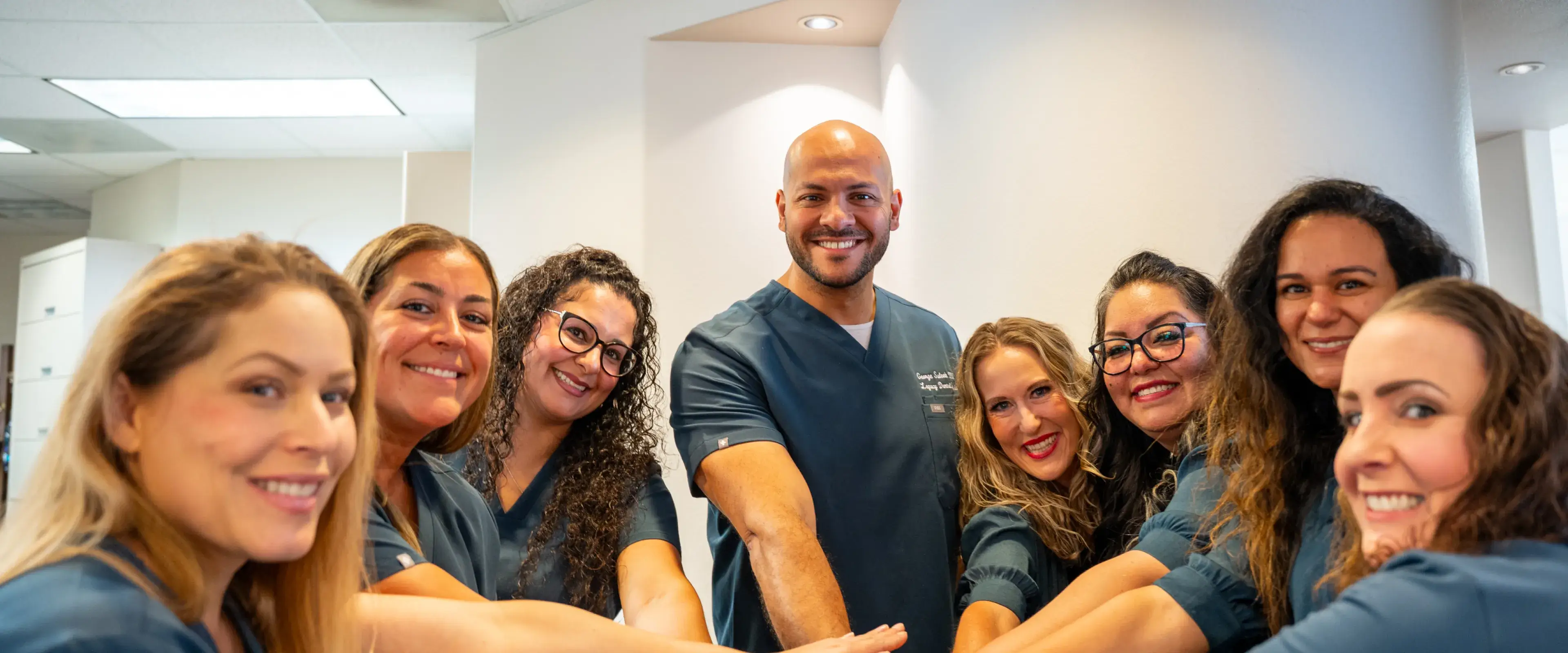 A group of smiling healthcare professionals standing together with hands joined in a unified gesture.