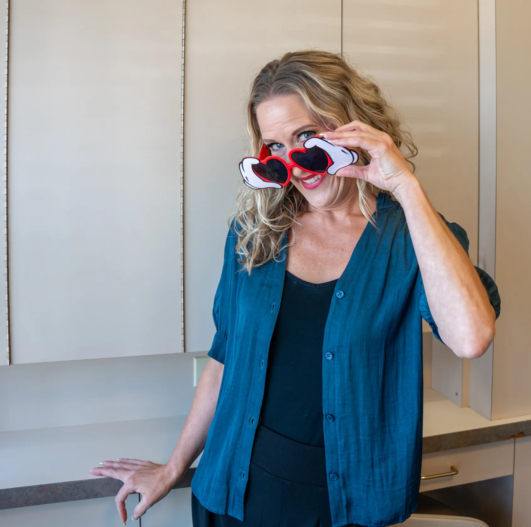Woman smiling and holding heart-shaped sunglasses over her eyes indoors.