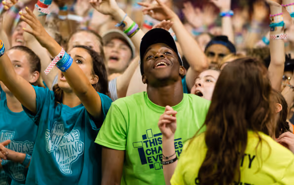 Young adults in bright shirts worshipping in a large group