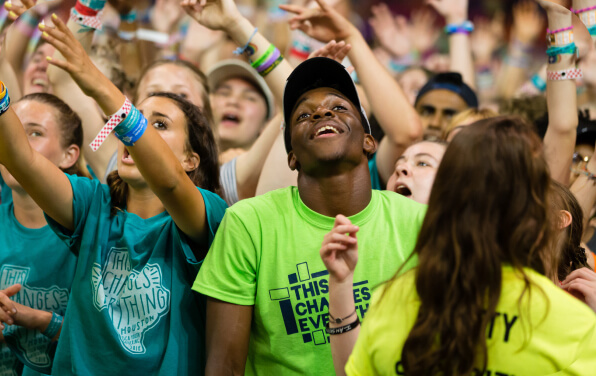 Young adults in bright shirts worshipping in a large group