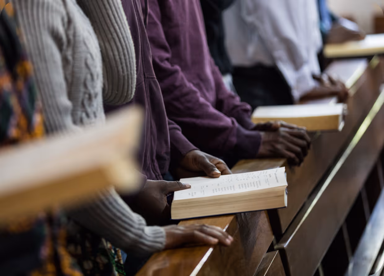 People standing in church pews holding open books during a worship service