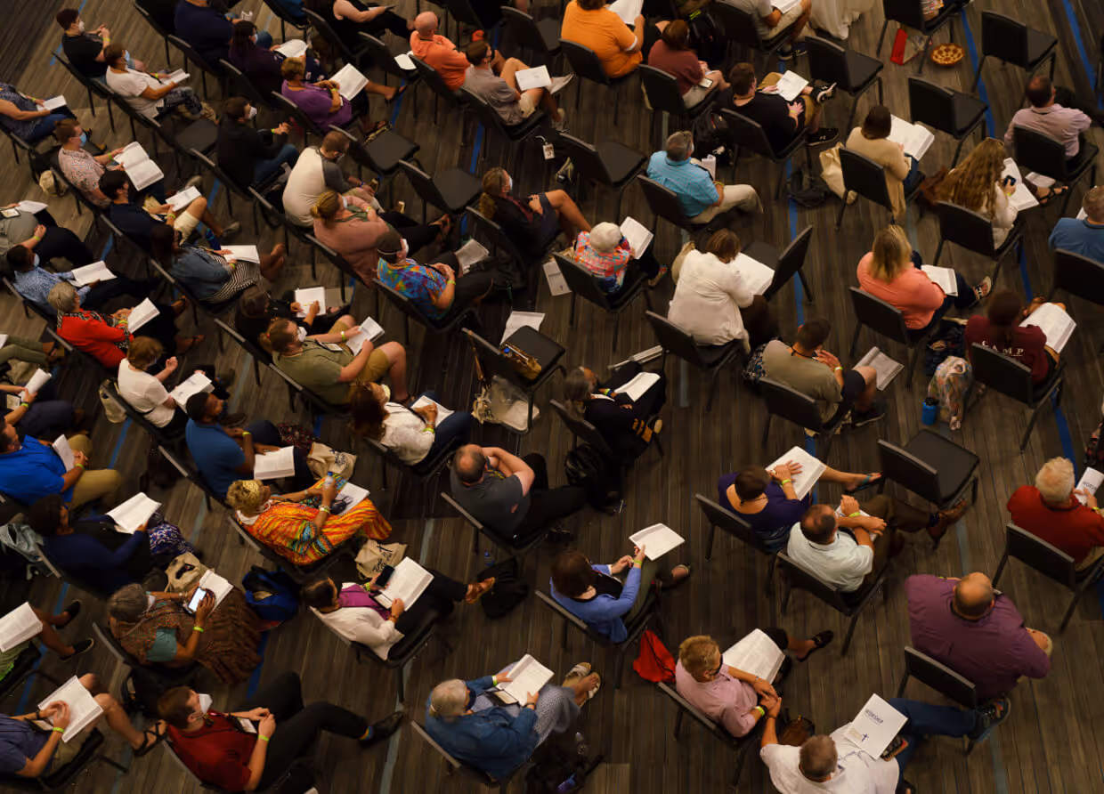Overhead view of people seated in rows reading documents during a large meeting
