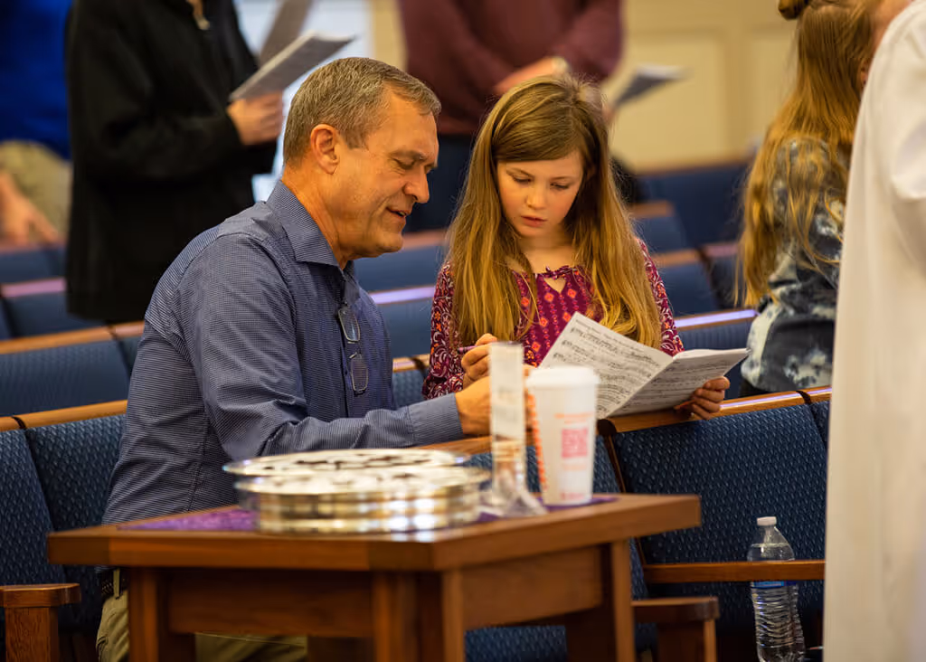 Adult and child reading a church bulletin together during a service