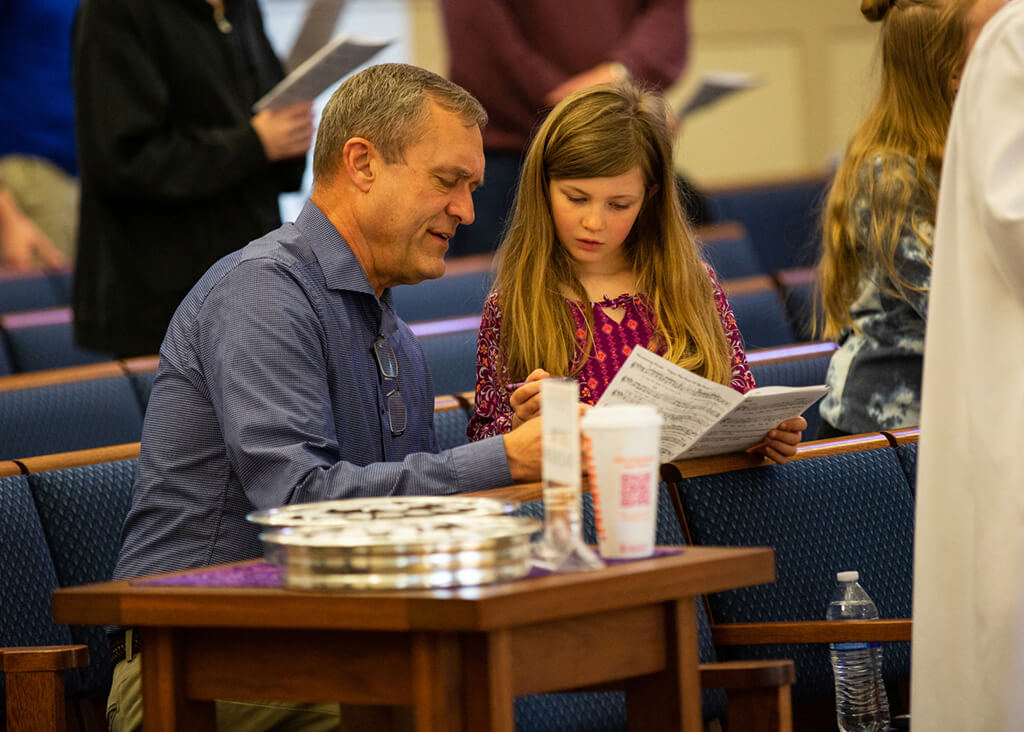 Adult and child reading a church bulletin together during a service