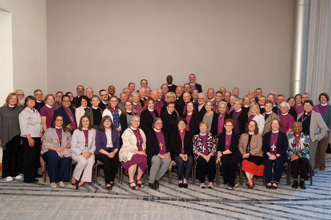 Group photo of 60 people seated and standing in rows, most wearing black and purple to signify their status as bishop of an ELCA Synod