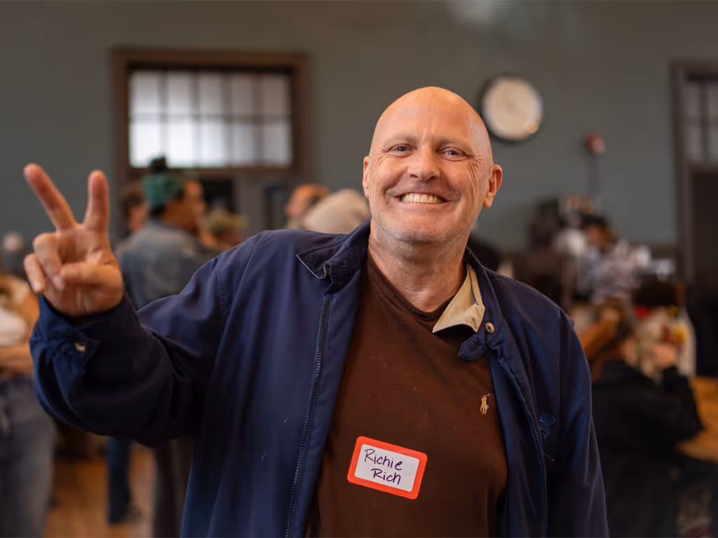 Man smiling and holding up two fingers in a crowded indoor space