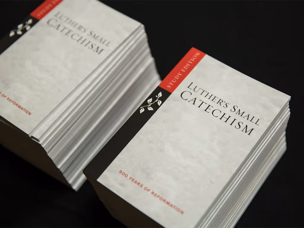 Two stacks of books with gray covers and black and red spines that say “Luther’s Small Catechism” on the front cover in black small caps serif font.