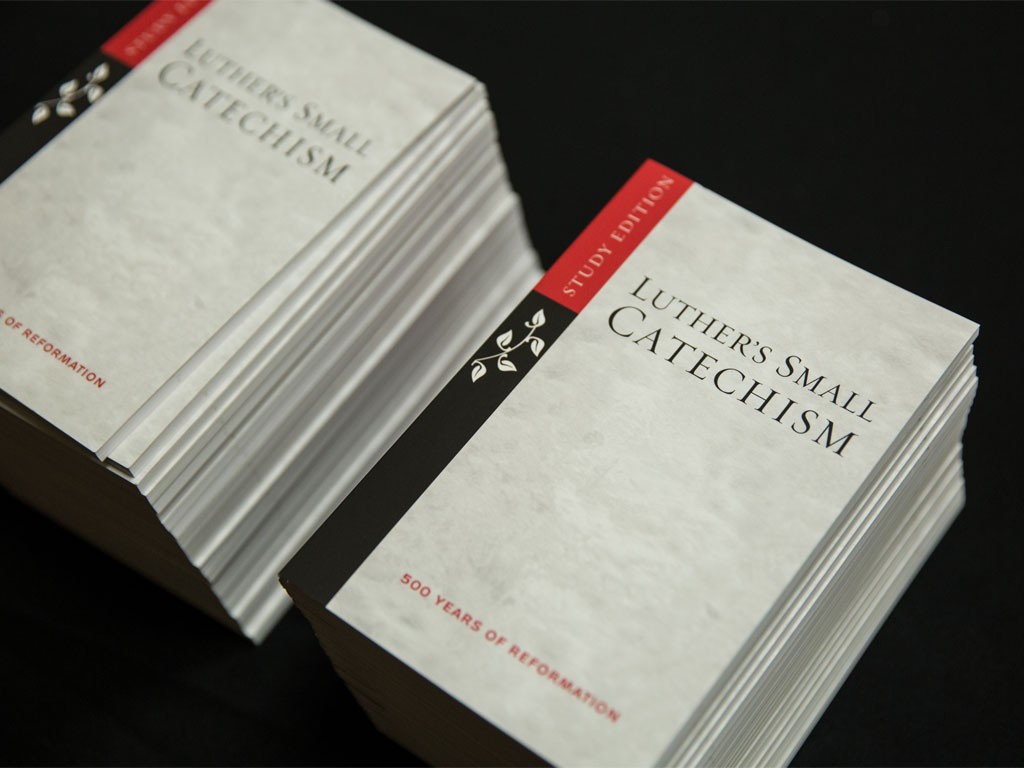 Two stacks of books with gray covers and black and red spines that say “Luther’s Small Catechism” on the front cover in black small caps serif font.