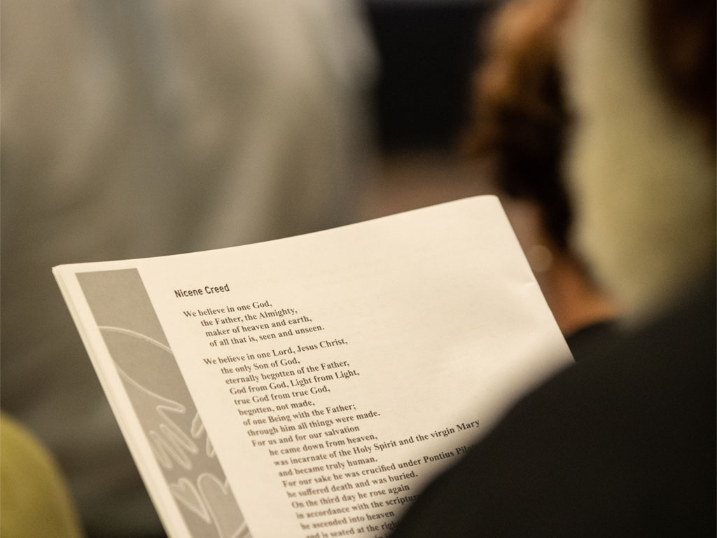 A person in black holds a printed copy of the Nicene creed as the camera looks over their shoulder to focus on the words.  