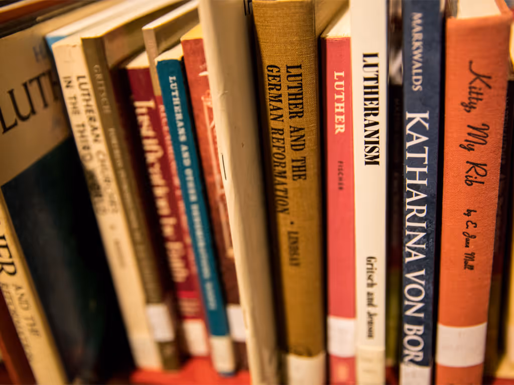 Various books of different sizes and colors on a shelf with spines facing the camera, most have “Luther” or “Lutheran” in the title.