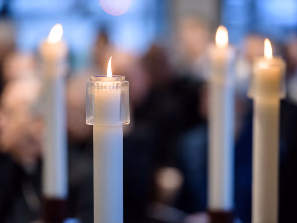 Four lit candles are arranged in a diamond. The one closest to the camera on the right is a pale yellow while the other three are white.