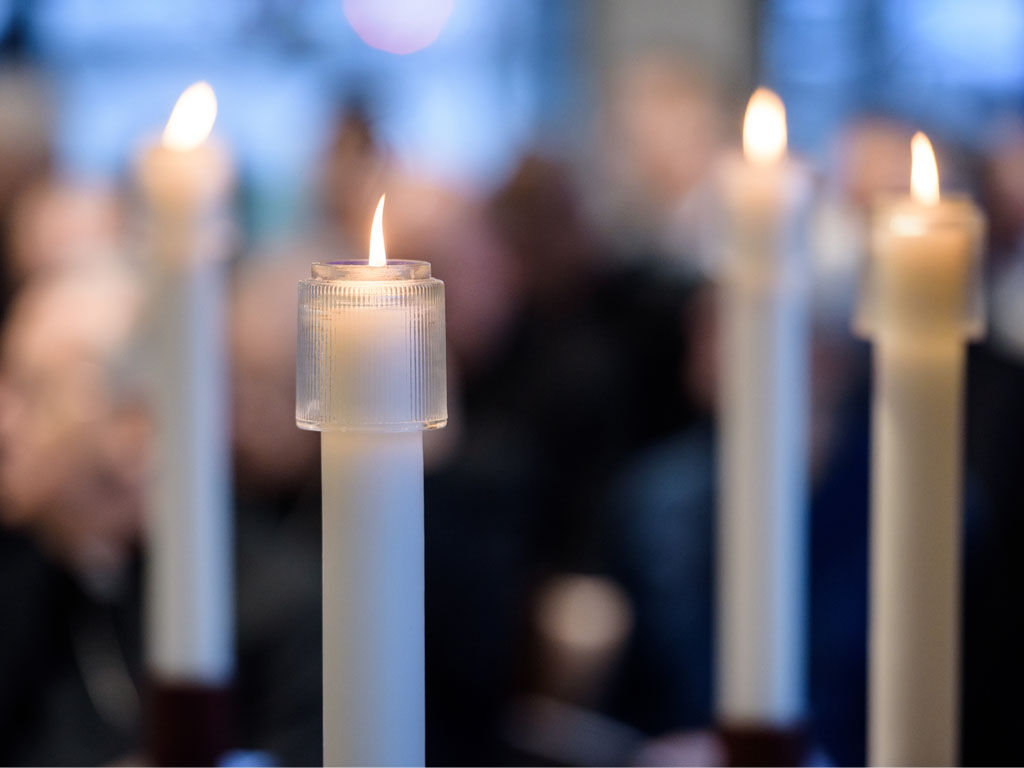 Four white candles arranged in a diamond pattern, all lit, with the one in the front right having a slightly darker color than the others.