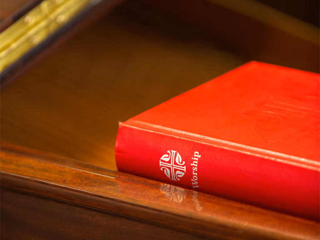 A red book with a cross and the word “worship” on the spine sits on a wooden table. 