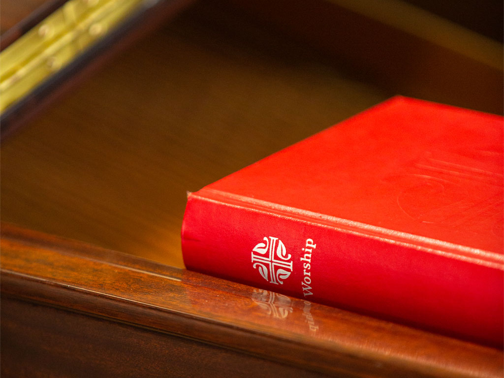 A red book with a cross and the word “worship” on the spine sits on a wooden table. 