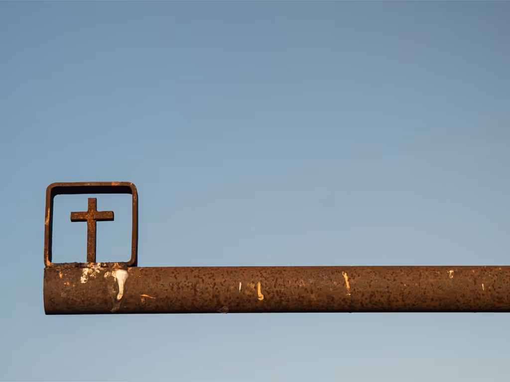 A long, rusted metal pole fills the screen entering from the right. On the far left side of the pole, a square with a cross is attached.