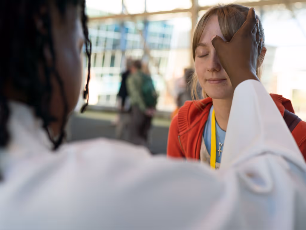 Person in a white robe makes the mark of the cross on the forehead of a female wearing a red sweater.
