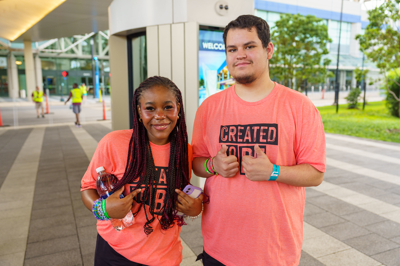Two young people stand outside New Orleans Convention Center, both wearing orange shirts while attending the 2024 ELCA Youth Gathering.
