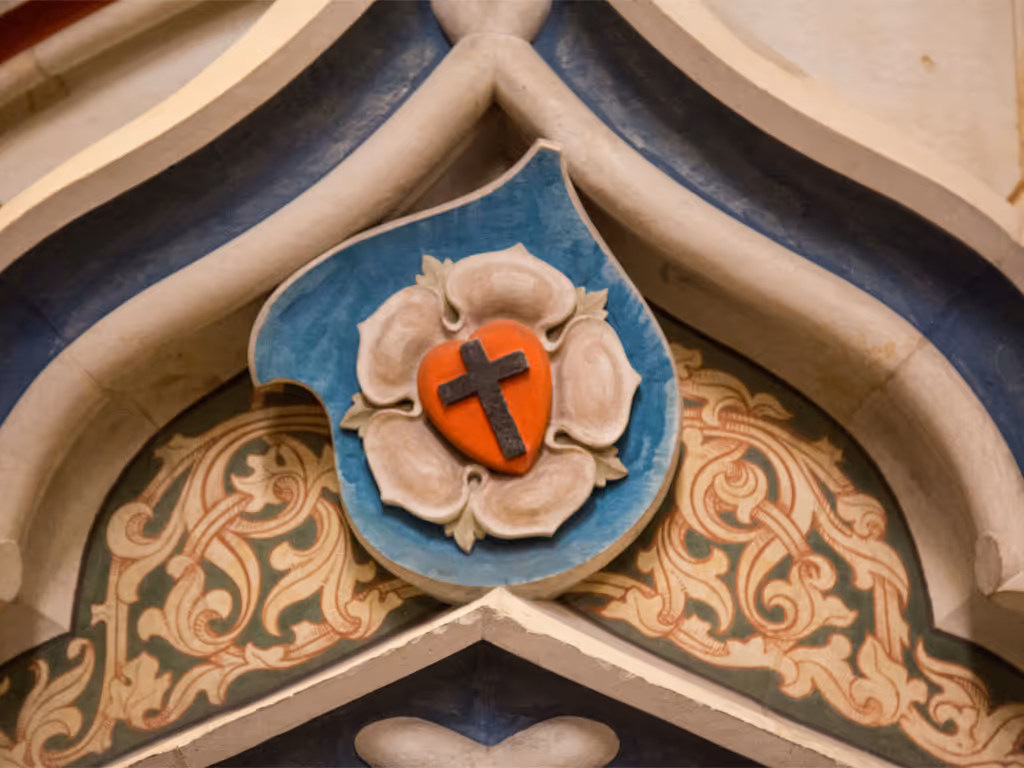 A relief carving, of a cross inside a heart inside a rose petal, sits at a corner in the masonry of the Schlosskirche in Wittenberg, Germany.  