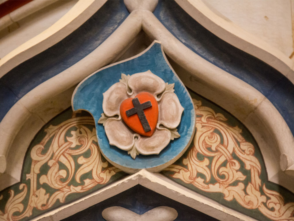 A relief carving, of a cross inside a heart inside a rose petal, sits at a corner in the masonry of the Schlosskirche in Wittenberg, Germany.  