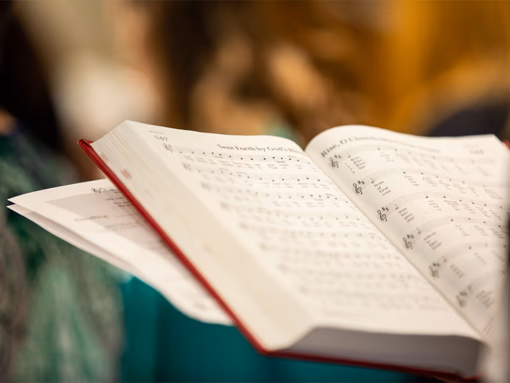 Red hyman open to two pages of songs, the one on the left titled “Sent Forth by God’s Blessing” with the nmber 547 in the top left corner.
