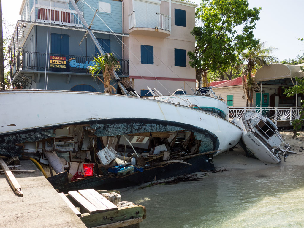 A long white boat sits on its side with a gaping hole in the hull showing large amounts of debris and trash after a storm.