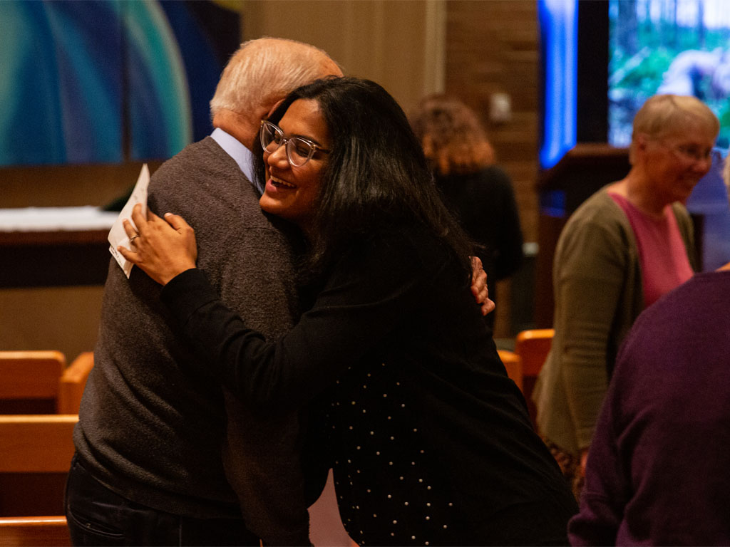 A woman in a black shirt embraces a man in a gray sweater inside a church. 