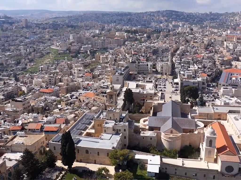 Aerial view of a city in Israel with short white buildings across the landscape opening to a mountain in the distance.